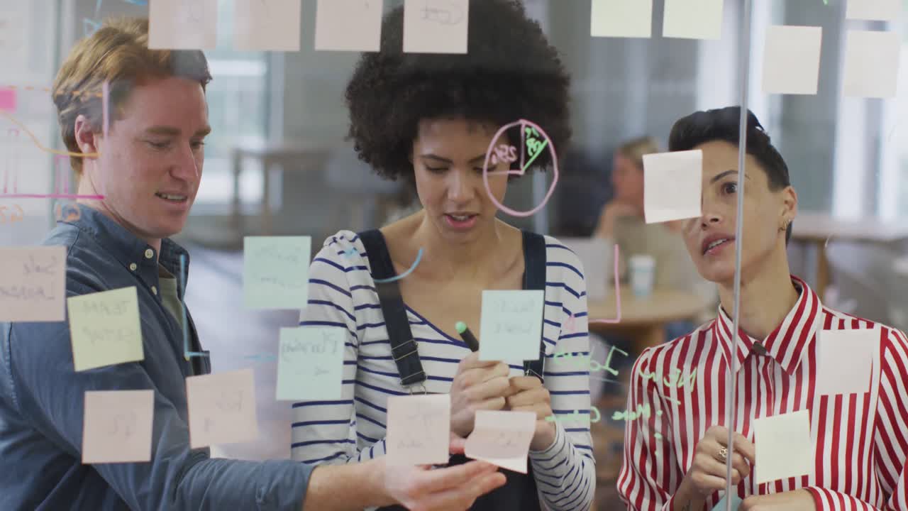 Diverse male and female business colleagues discussing by glass wall with memo notes