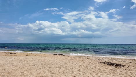 A-wide-shot-of-a-sandy-beach-in-Crimea,-Russia,-with-the-blue-ocean-in-the-distance-and-a-clear-blue-sky-with-white-clouds-overhead