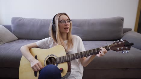 mujer con auriculares toca la guitarra en su casa, divirtiéndose felizmente tocando la guitarra y cantando