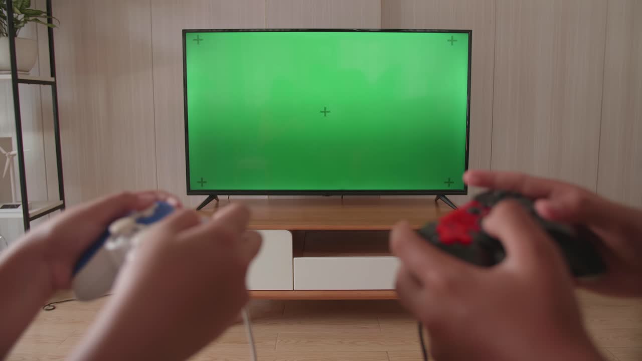 Primo piano delle mani di bambini che tengono un joystick e giocano a un videogioco su una TV con schermo verde