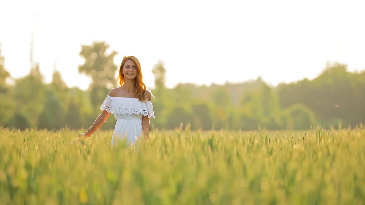 Beautiful woman walks in the field, the girl smiles. Field with wheat in summer. Circular motion of the camera.