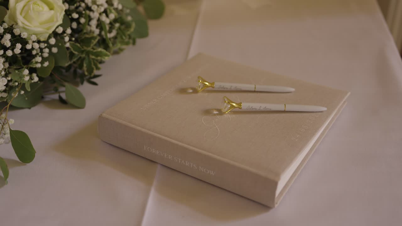 Wedding guestbook with pens and white floral arrangement – elegant reception table detail