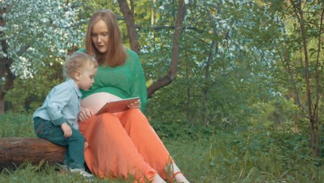 Pregnant-mother-and-son-with-tablet-PC-outdoor