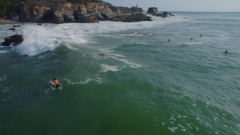 Vista-Aérea-Panorámica-A-Través-De-Los-Surfistas-Montando-Olas-En-Punta-Zicatela-Oaxaca-Iluminada-Por-El-Sol-Paisaje-Marino-Del-Océano-Pacífico