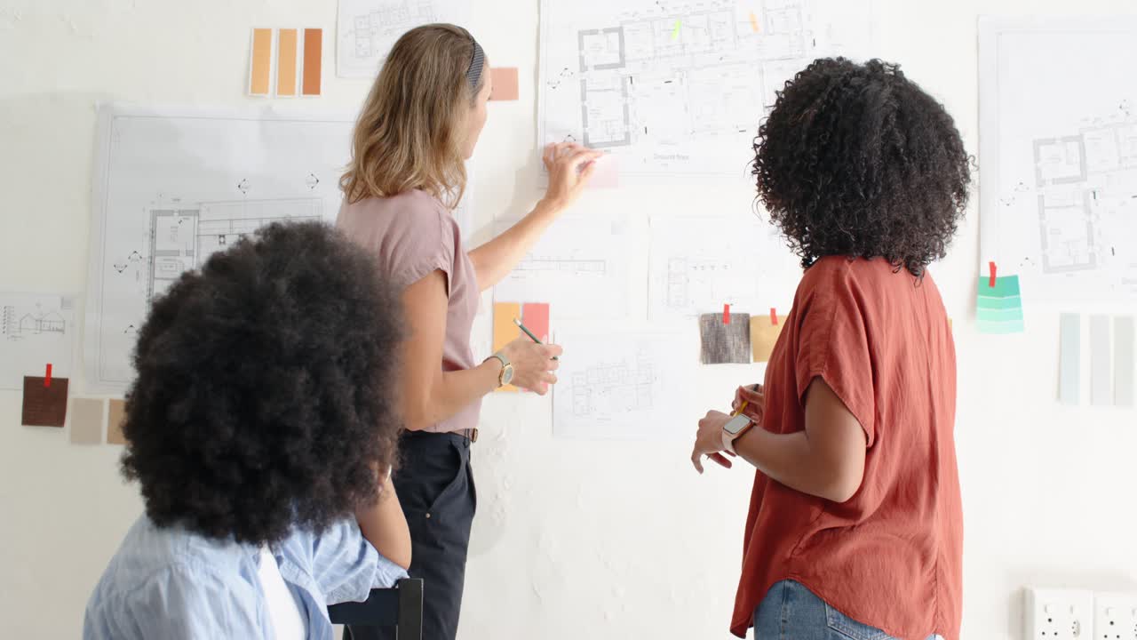Diverse women team checking plans swatches pinned at studio after seated woman gesture with pencil