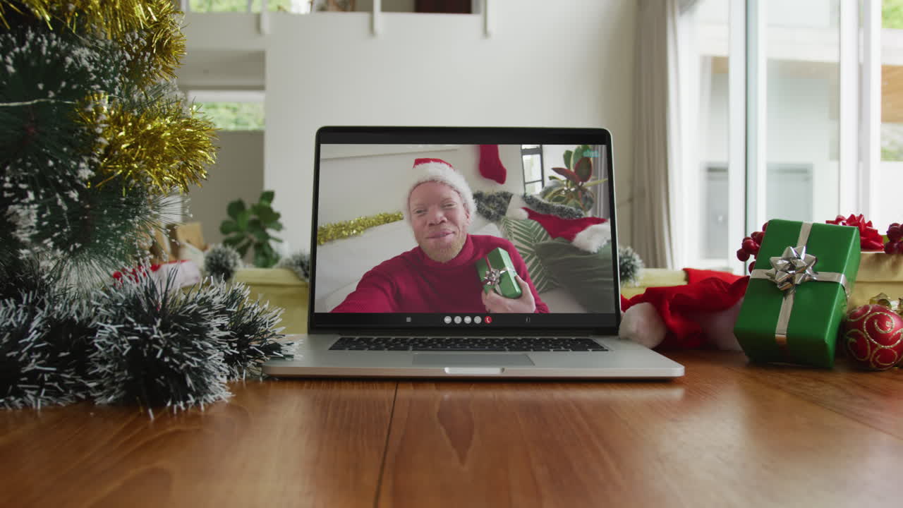 hombre afroamericano albino sonriente con sombrero de papá noel en una videollamada en una computadora portátil