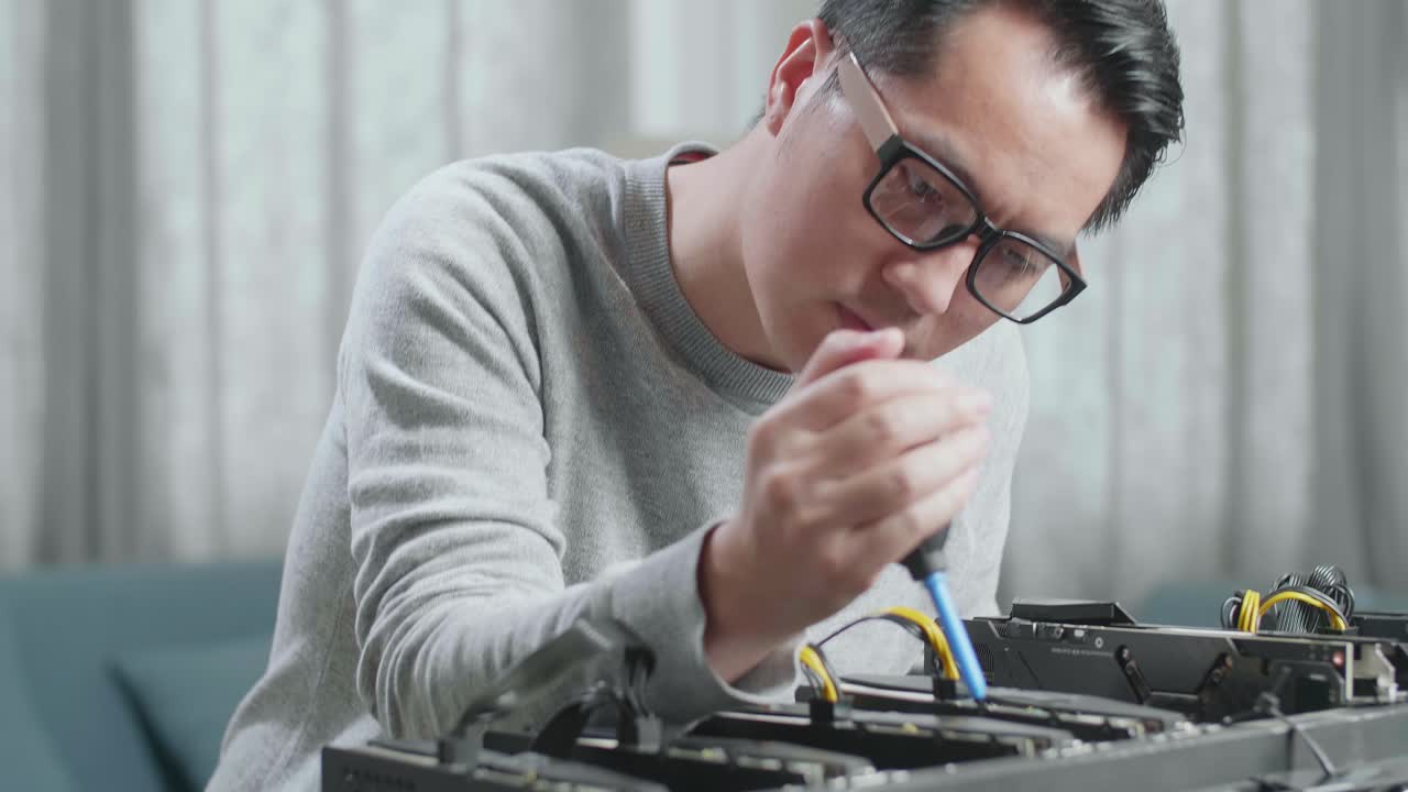 안경을 쓴 아시아 남자가 암호화폐를 채굴하기 위해 광산 기계를 청소합니다.