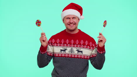 Funny-man-in-red-New-Year-sweater-holding-candy-striped-lollipops-hiding-behind-them,-fooling-around