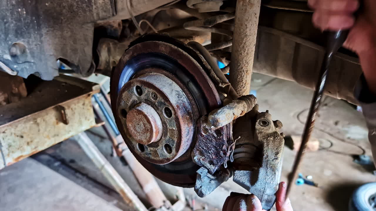 Mechanic uses screwdriver to loosen and remove rusty brake caliper from brake disk