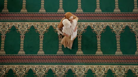 two muslim women hugging in a mosque