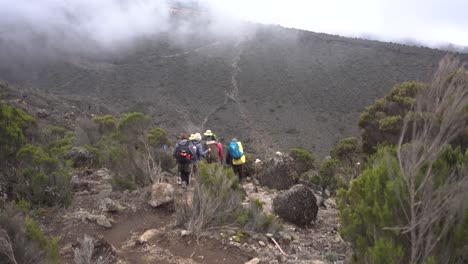 Schwenk,-Der-Wanderer-Zeigt,-Die-Mit-Ausrüstung-Den-Kilimandscharo-Hinuntergehen,-Mit-Wolken-Im-Hintergrund