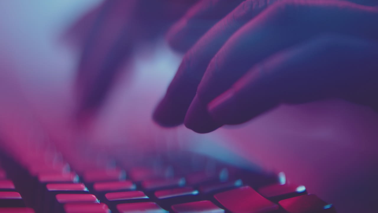 Hands typing on a keyboard under vibrant neon lights