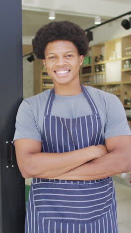 vertical video of smiling african american male barista wearing apron in cafe