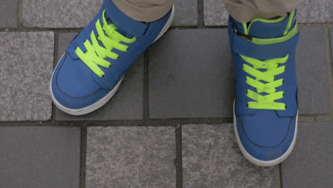 kid feet in blue trainers on paved sidewalk