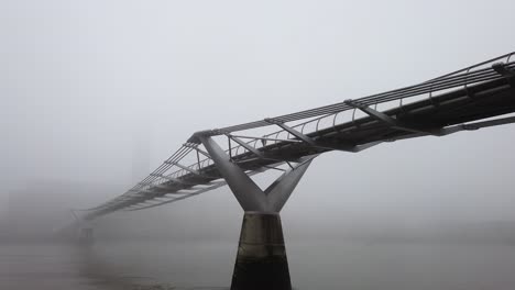 people crossing london's millennium bridge shrouded in thick fog