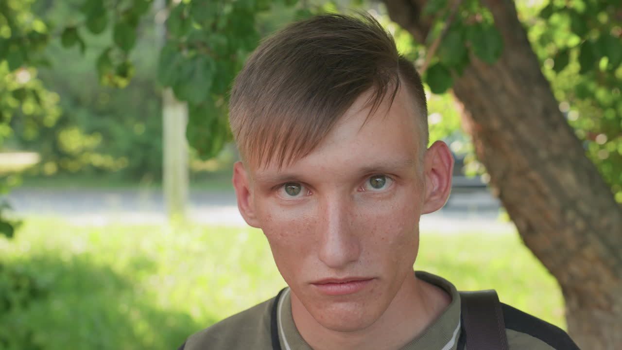 White Man Portrait At Roadside, Cautious Stare Toward Traffic, Backpack Visible, Hot Summer Light, Anxious Commuter Vibe With Paranoid And Wary Mood, Close Urban Scene Capturing Uneasy Observation
