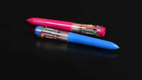 two pens with colored refills on a black. ten different colors. side view. loop motion. rotation 360.