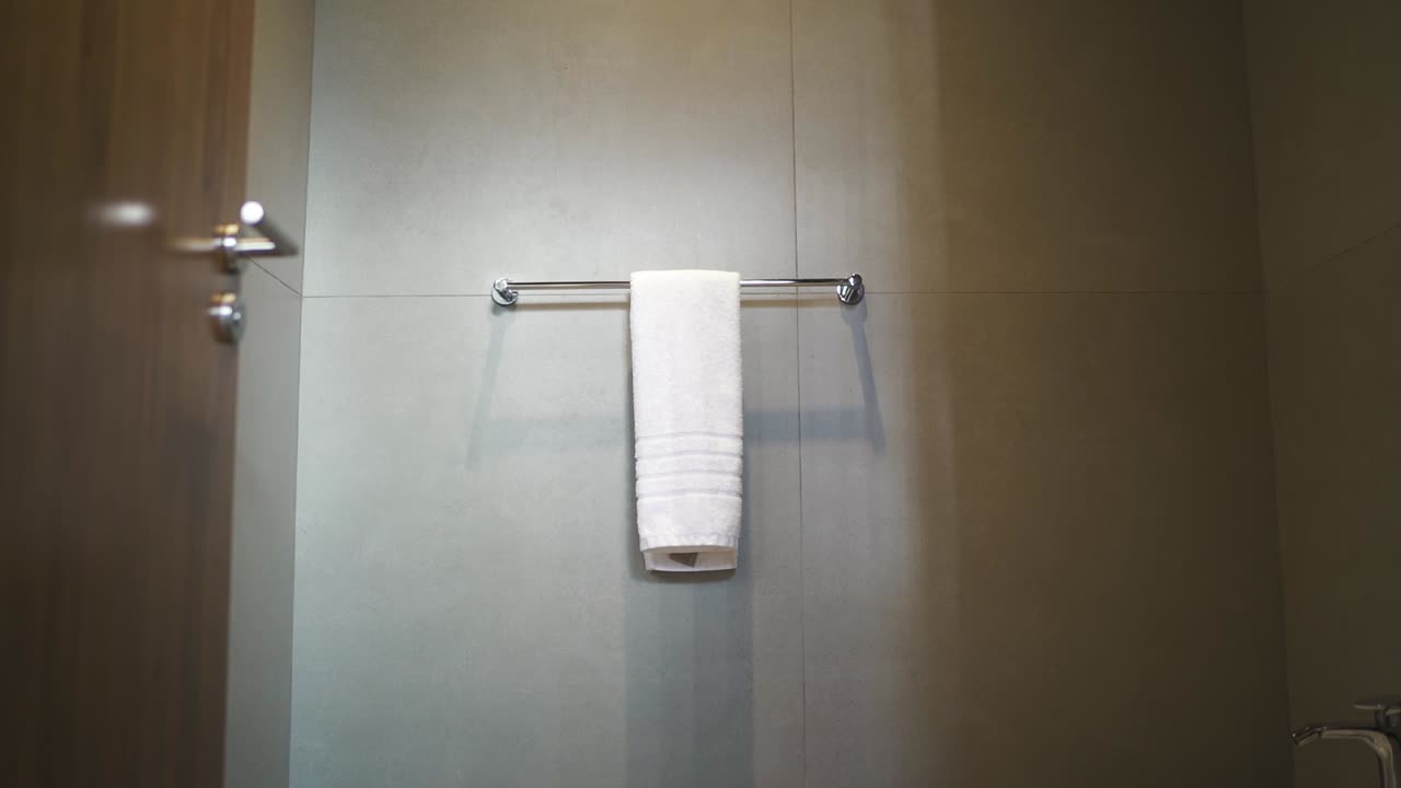 A clean hotel bathroom with modern fixtures and bright lighting, showcasing a single folded hand towel on dowel