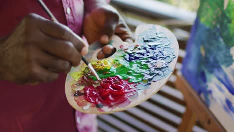 midsection of african american senior man using paint palette, painting picture on canvas