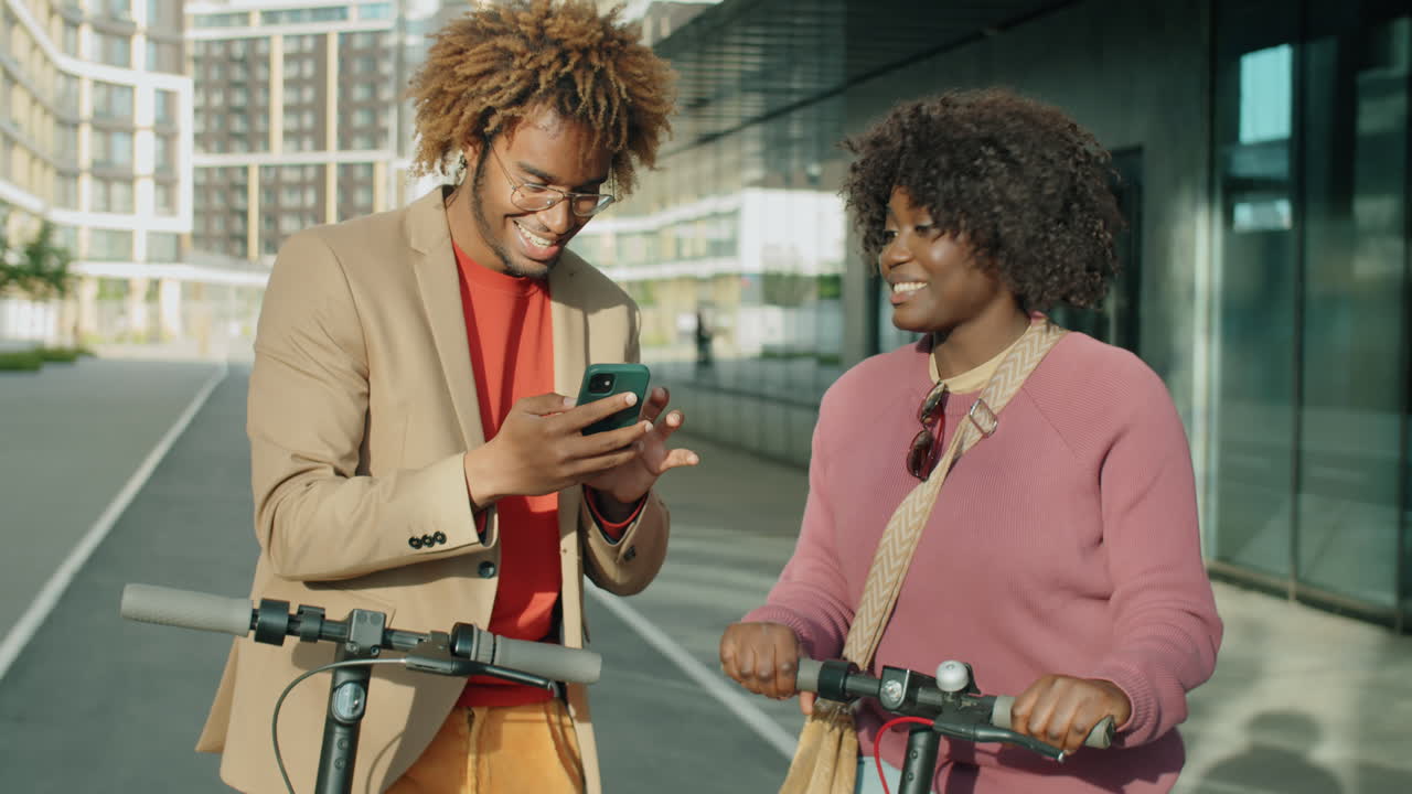 African American Man and Woman with E-Scooters Using Phone and Talking on Street
