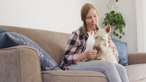 caucasian woman playing with her dog while sitting on the couch at home