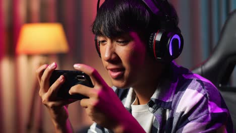 close up of excited asian teen boy gamer celebrates victory while playing video game on smartphone