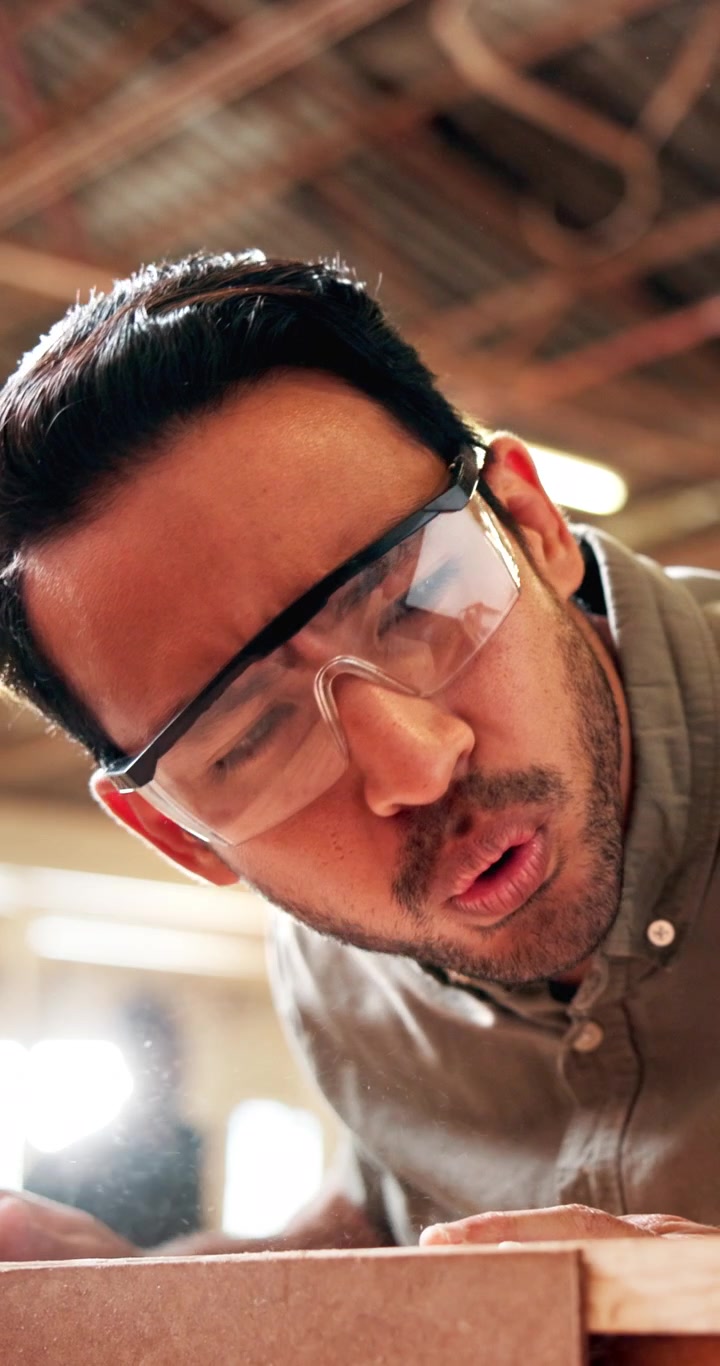 Carpenter Wearing Safety Glasses Blowing Sawdust Off Wood Plank