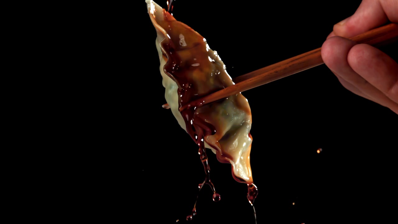 Salsa di soia che gocciola al rallentatore su un raviolo tenuto con le bacchette