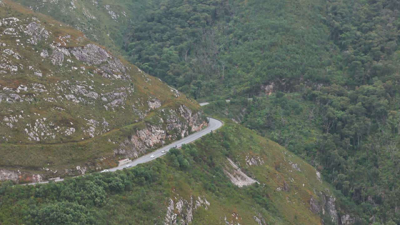fotografía aérea de varios coches conduciendo a lo largo de la carretera sinuosa en outeniqua pass, cabo occidental, sudáfrica. la carretera se curva a través de un paisaje exuberante y verde, ofreciendo una impresionante vista de las montañas