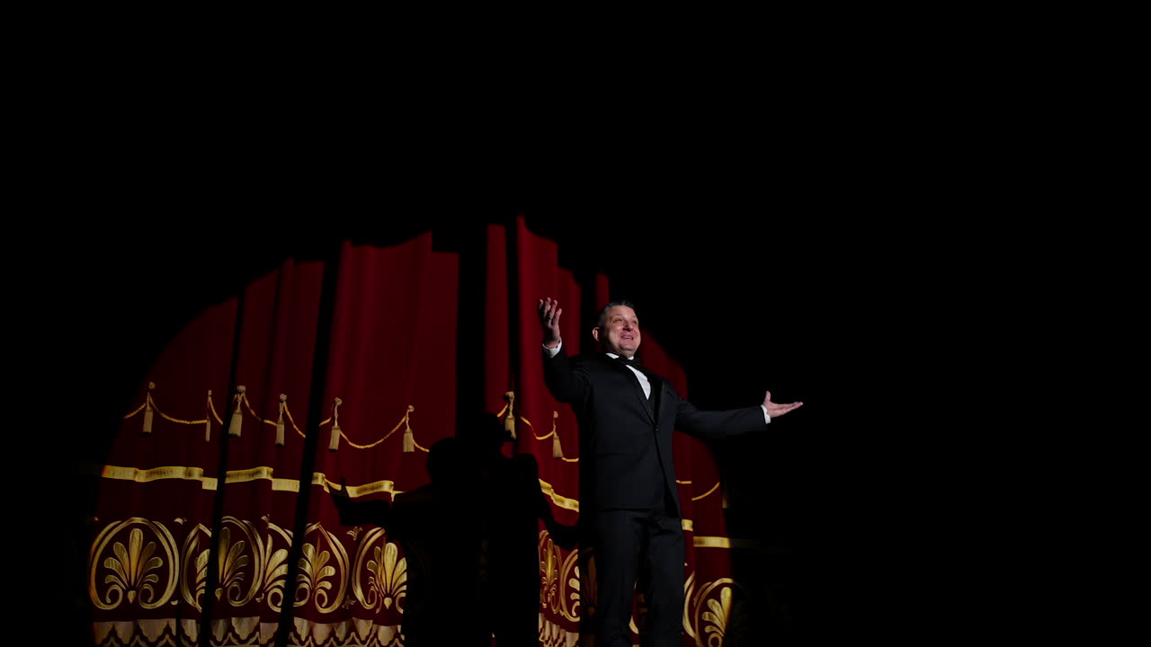Male performer on stage. Actor in elegant suit presenting the performance in the theater. Comedian appears on the scene. Light spot on dark background.