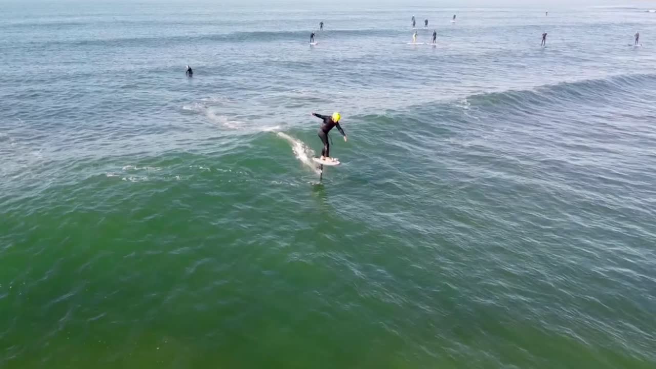 Riding ocean waves with foil drive powered on, aerial view from behind on a clear summer day, gliding along the European coastline, connecting wave after wave.