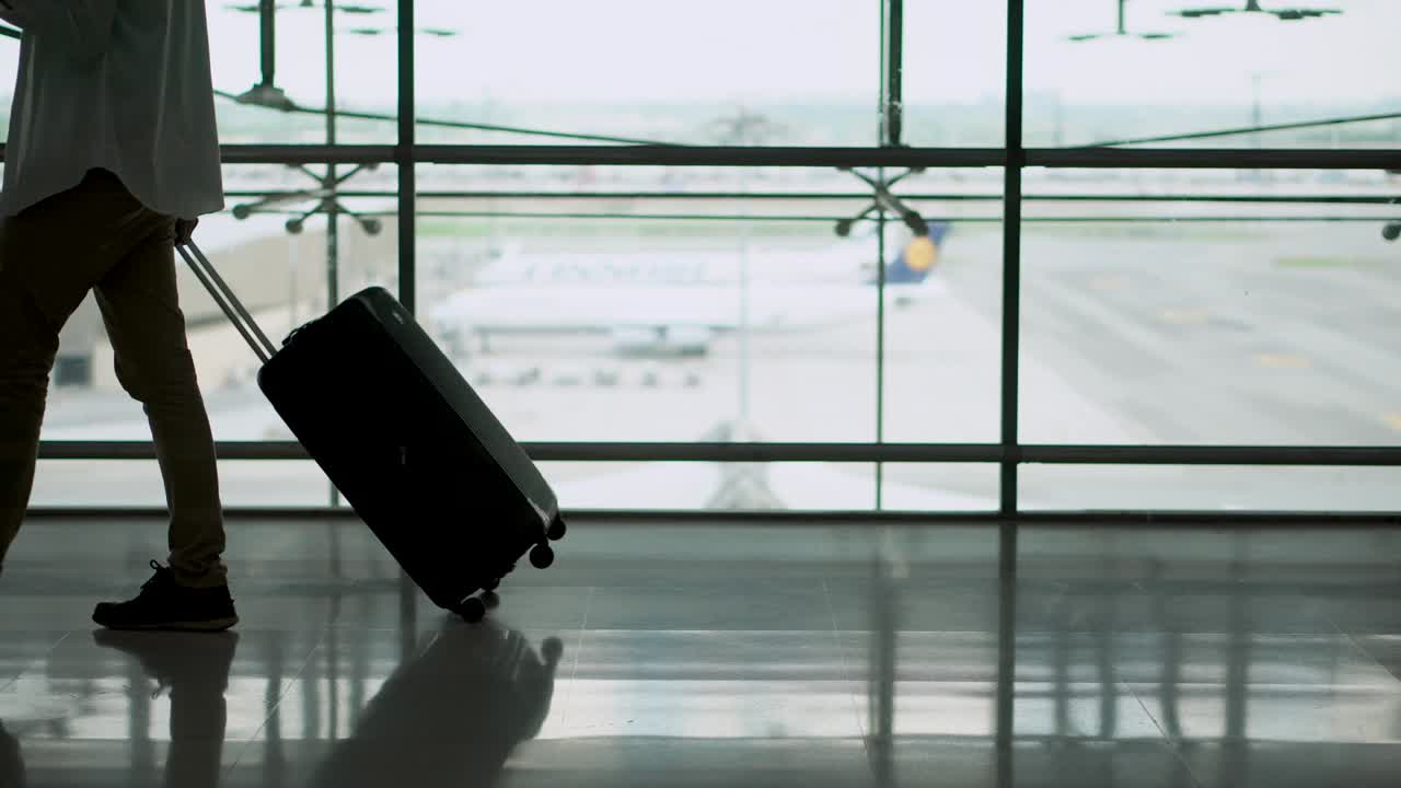 Joven pasajero caminando con su maleta en la zona de salidas de la terminal del aeropuerto. Empresario asiático con ropa informal en viaje de negocios. Conceptos de estilo de vida de viaje moderno