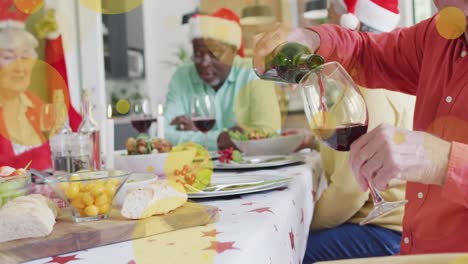 Animation-Von-Gelben-Lichtflecken-über-Einem-Kaukasischen-älteren-Mann,-Der-Am-Weihnachtstisch-Wein-Einschenkt