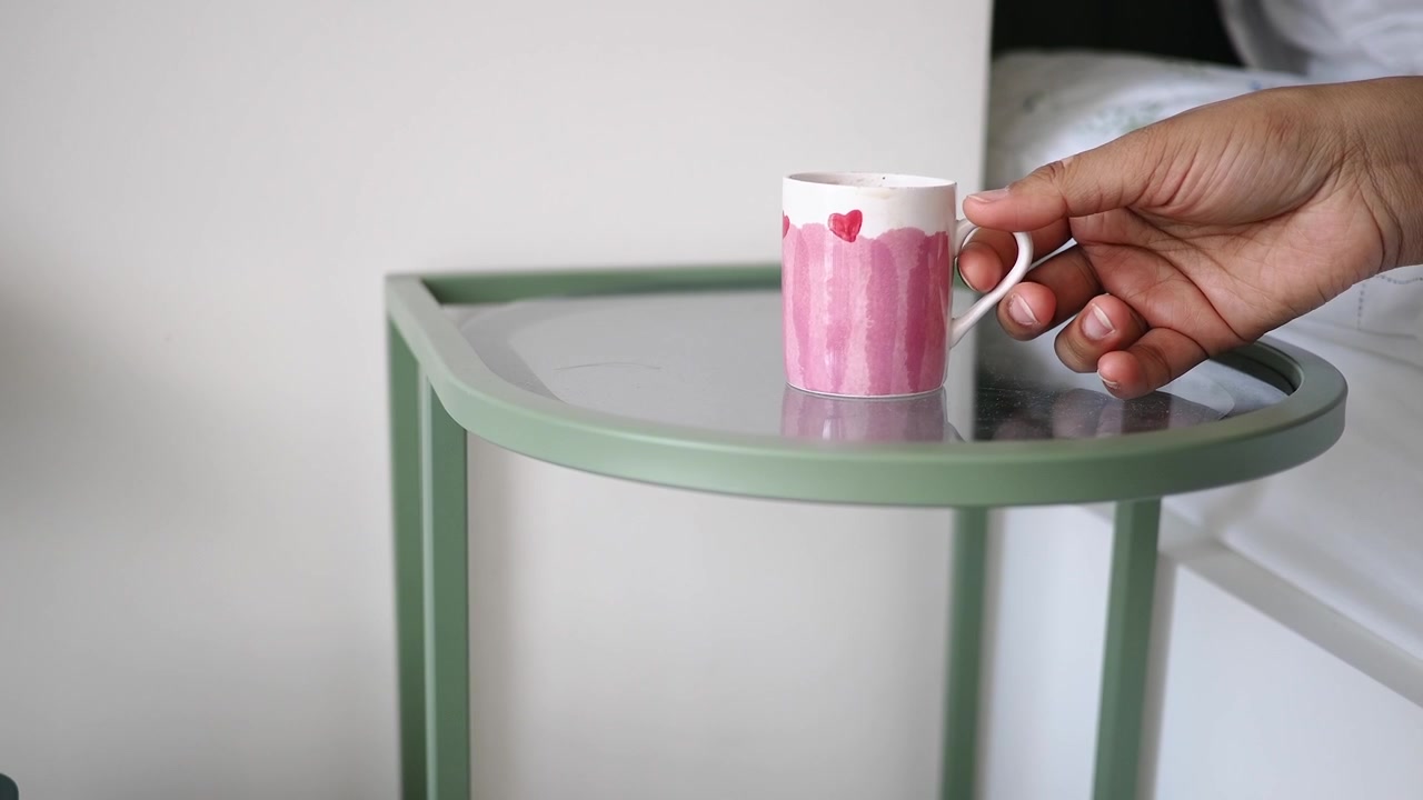 Mano che prende una tazza rosa con motivo a cuore da un tavolino laterale di vetro
