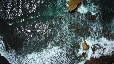 Toma-Aérea-De-Arriba-Hacia-Abajo-De-Las-Olas-Del-Océano-Chocando-Contra-Las-Rocas-De-Coral-En-Indonesia