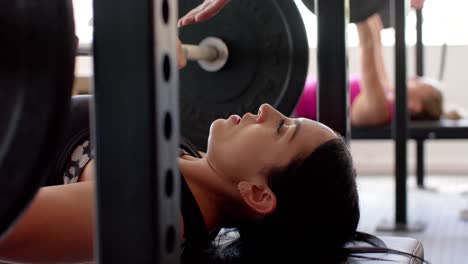 determined unaltered biracial woman weight training at gym bench pressing barbell, in slow motion