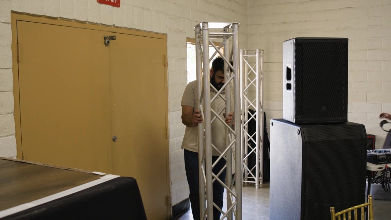 Un uomo costruisce tralicci in alluminio all'interno di una location per eventi mentre prepara l'attrezzatura per luci e audio per una quinceañera