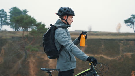 männlicher radfahrer trinkt wasser und ruht sich vom mountainbiken auf dem hügel aus