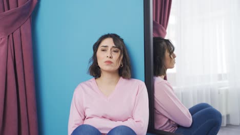 una joven deprimida e infeliz llorando frente al espejo.