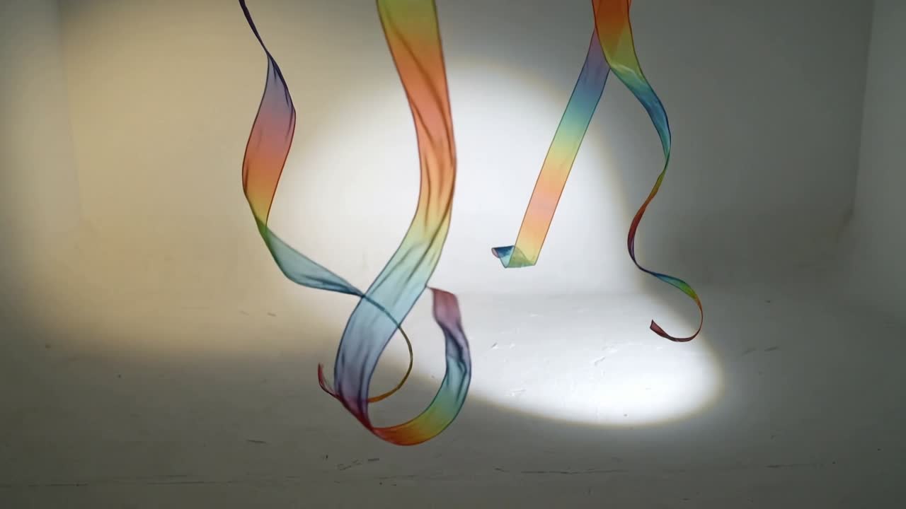 Twisting and curling three rainbow ribbons responding to appearing beam in studio, casting shadows