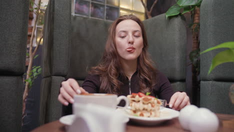 lady enjoys delicious waffles while leaning back comfortably in cozy booth, sipping latte beside decorative plants and warm interior elements, capturing moment of relaxed indulgence and satisfaction