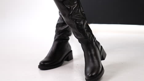 beautiful elegant stylish female boots presentation. lady turning and showing fashionable footwear at white floor backdrop. close up.