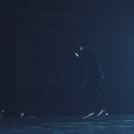talented young dancer dancing hip hop street dance on a stage in front of the spotlight. back view of a man dancing to the audience in the club.
