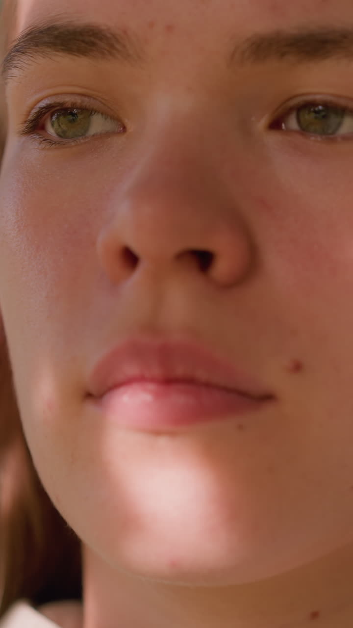 Close-up of young lady gazing intently with sunlight reflecting softly on her face, creating a serene and focused expression, background is beautifully blurred with green hues