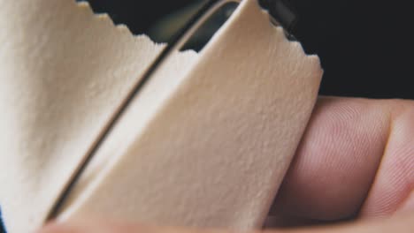 person cleans glasses with beige napkin on dark background