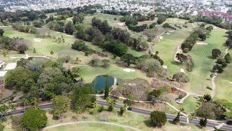 Vista-Aérea-Del-Campo-De-Golf-Jugadores-Profesionales-Practicando-El-Deporte,-Ciudad-De-Fondo