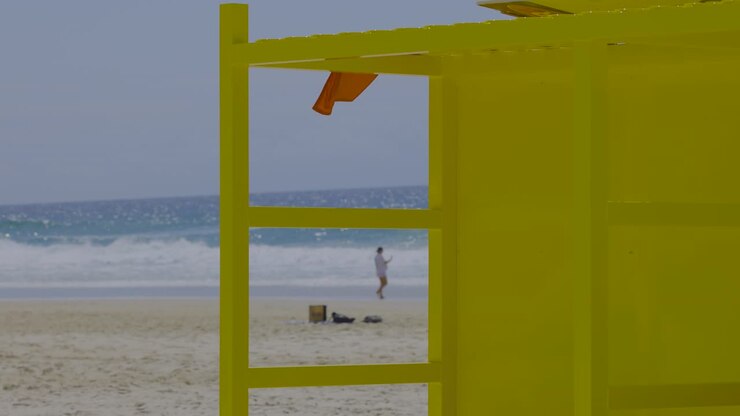 Persona caminando cerca de una estructura amarilla en la playa