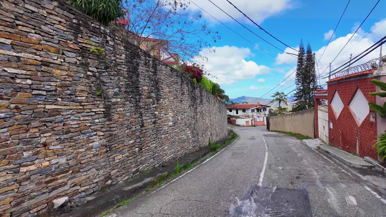 Tranquilla strada residenziale collinare con case, vegetazione e vista sulle montagne in lontananza a San Antonio de Los Altos, Venezuela