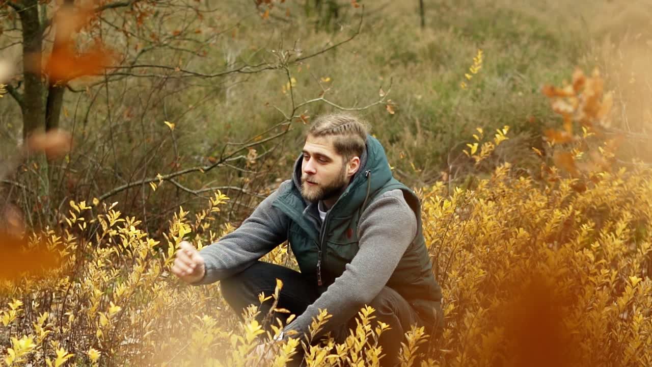 Mand sidder på en mark med gule blomster, mens han ryger tobak.