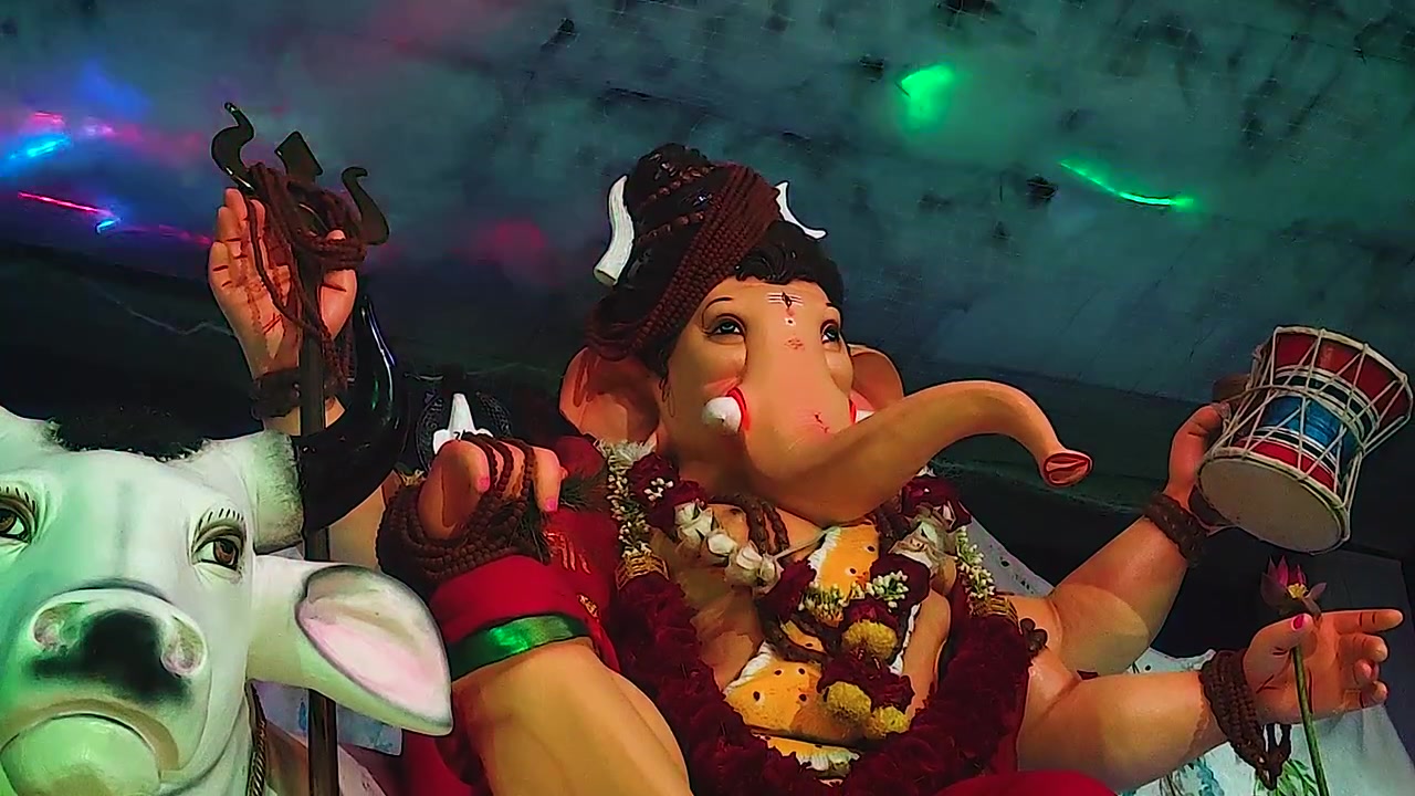 Idolo di Ganesh vestito come Lord Shiva seduto vicino al toro Nandi, un'inquadratura dal basso rivela un effetto di fulmini al neon verde nel soffitto decorato a nuvole durante il Ganesh Chaturthi in India